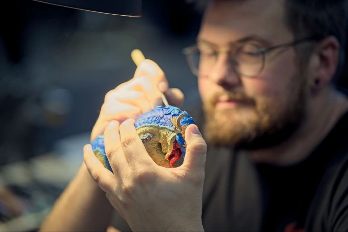 Close up of artist painting detailed blue dragon miniature figurine