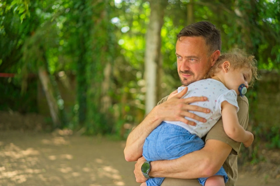 Father holding sleeping toddler daughter on shoulder outdoors in natural light