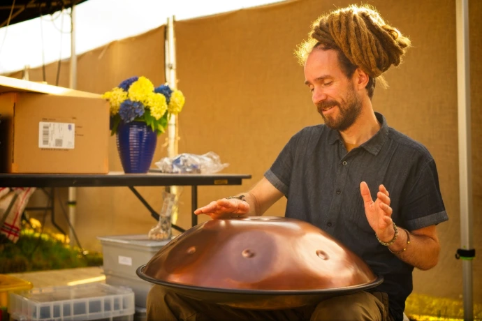 Musician with dreadlocks playing handpan drum at outdoor festival